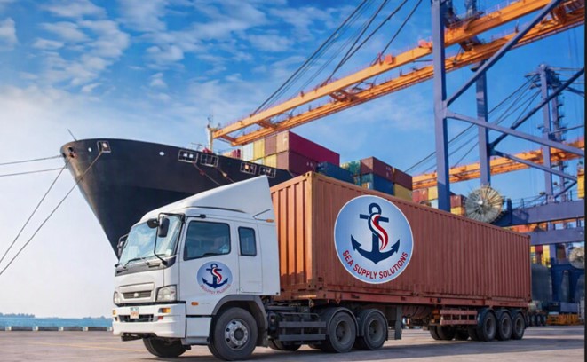 Caminhão da Sea Supply Solutions em terminal portuário, com navio, contêineres e guindastes ao fundo
